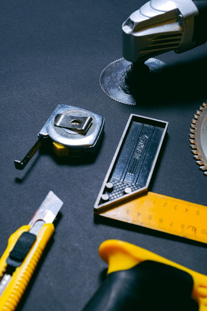 why-choose-us Assorted hand tools including a tape measure, utility knife, and saw blade on a dark background.